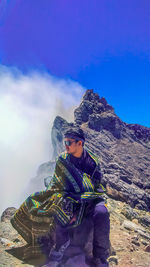 Young man sitting on mountain against sky