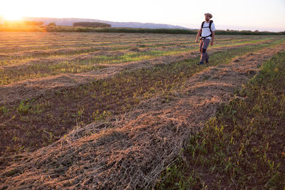 Man walking on land against sky during sunset