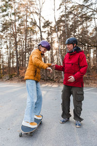 Father holding hand of teenage daughter riding skateboard in autumn park during weekend