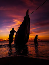 Silhouette people on beach against sky during sunset