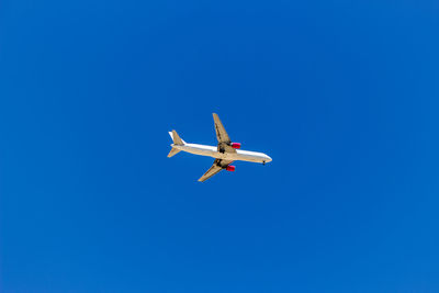 Low angle view of airplane flying against clear blue sky