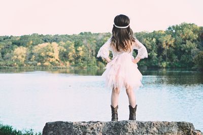 Rear view of girl standing by lake against sky