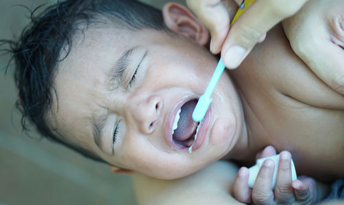 Close-up of hand brushing teeth of crying boy