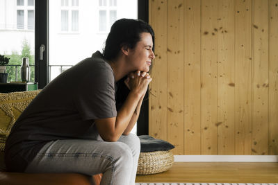 Side view of depressed woman grimacing while sitting on sofa at home