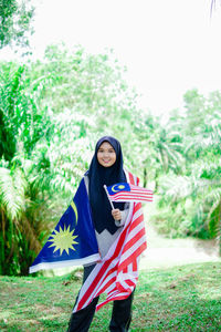 Portrait of young woman standing against trees