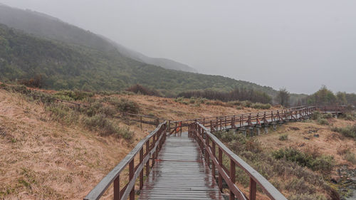 Footbridge leading towards mountains against sky