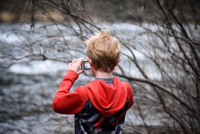 Rear view of boy photographing lake through digital camera