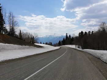 Empty road by snowcapped mountains against sky