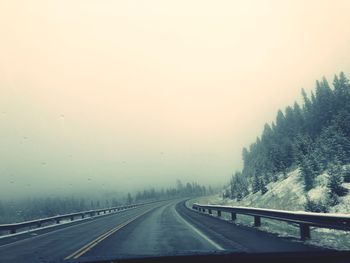 Road by trees against sky during winter