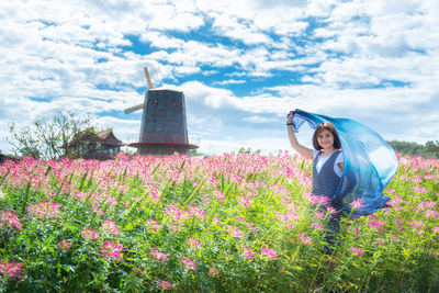 Portrait of woman with scarf standing by blooming flowers against sky