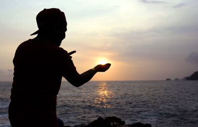 Silhouette man standing by sea against sky during sunset