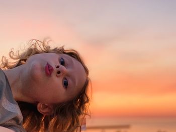 Close-up portrait of girl puckering at beach against sky during sunset