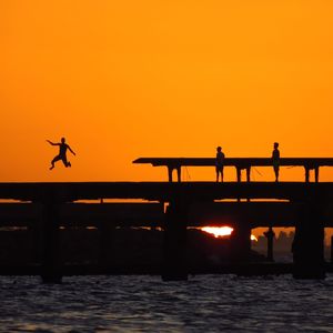 Silhouette people in sea against orange sky