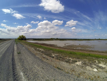 Empty road amidst field against sky