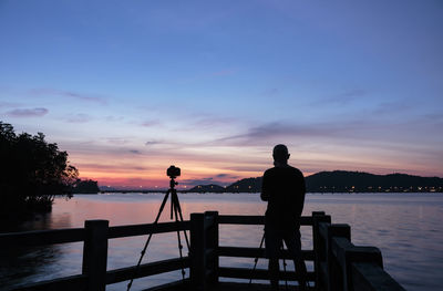 Silhouette man photographing sea against sky during sunset