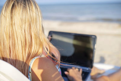 Rear view of woman using laptop at beach