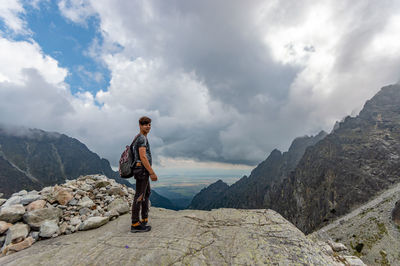 Side view of teenage boy standing on mountain against cloudy sky