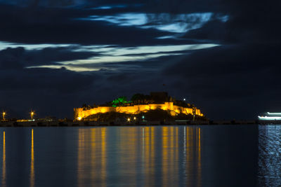 Illuminated city by sea against sky at night
