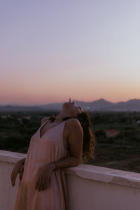 Rear view of woman standing on rock against sky during sunset