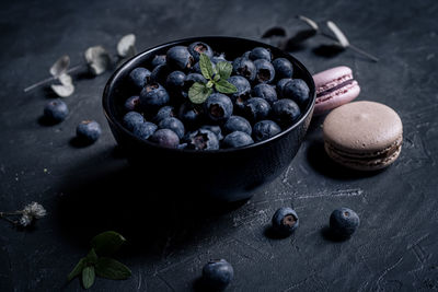 Close-up of fresh blueberries in a black bowl with macaroons around on a black slate.