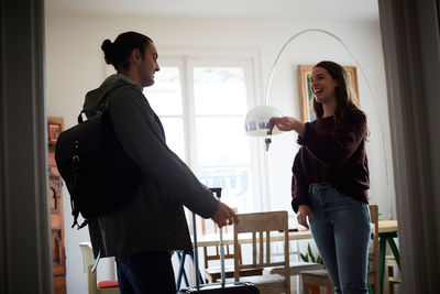 Smiling woman holding keys while talking to man in apartment on sunny day