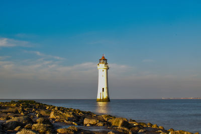 Lighthouse by sea and buildings against sky