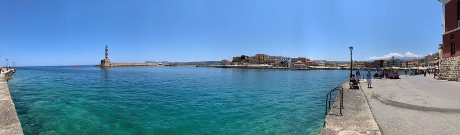 Panoramic view of buildings by sea against clear blue sky