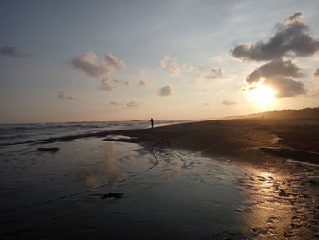 Mid distance view of person standing on shore against sky during sunset