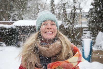 Cheerful mature woman wearing knit hat and scarf while snowing in winter