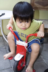 Cute smiling boy sitting on tricycle at home