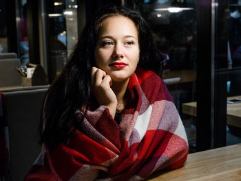 Young woman wrapped in blanket sitting at restaurant