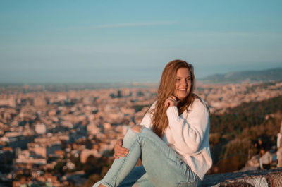 Smiling young woman looking away while sitting against sky