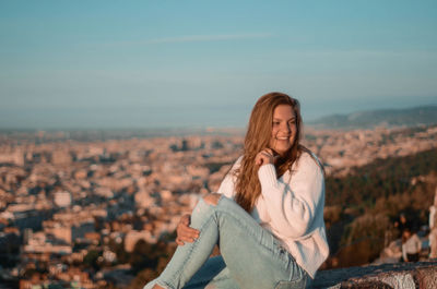 Smiling woman sitting outdoors against sky