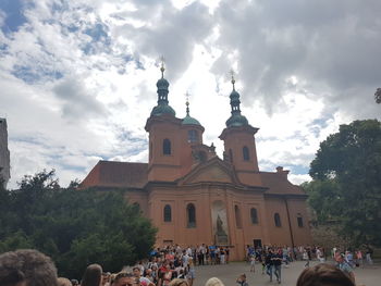 People walking in front of church against cloudy sky