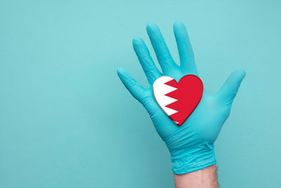 Close-up of hand holding heart shape against blue background