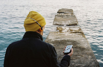 Rear view of man listening to music with an old walkman near the coastline 