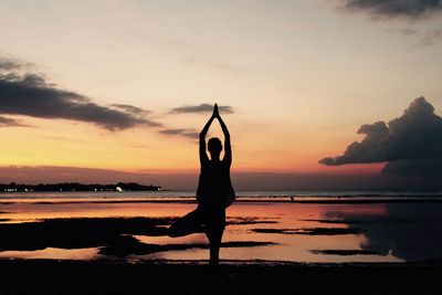 Silhouette woman meditating at beach against sky during sunset