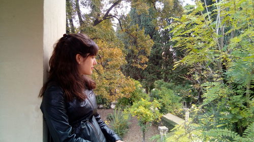 Side view of young woman standing by tree