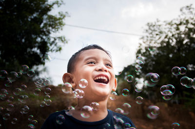 Close-up of cheerful boy with bubbles against sky