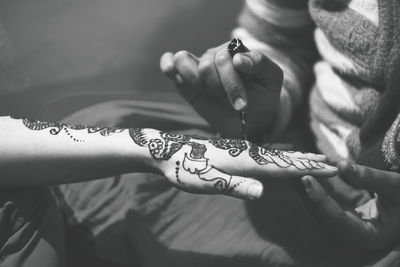 Midsection of woman applying henna on cropped hand