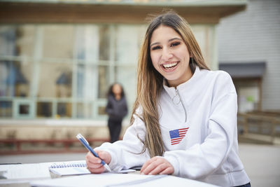 Portrait of smiling teenage girl sitting at table in schoolyard