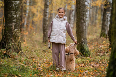 Portrait of young woman standing by tree trunk in forest