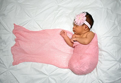 Directly above shot of baby girl wrapped in pink fabric sleeping on bed