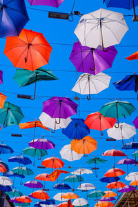 Low angle view of umbrellas hanging against blue sky