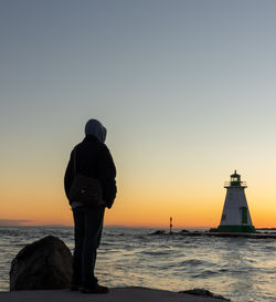 Rear view of man standing by sea against clear sky during sunset