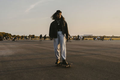 Young woman standing on skateboard against sky in park