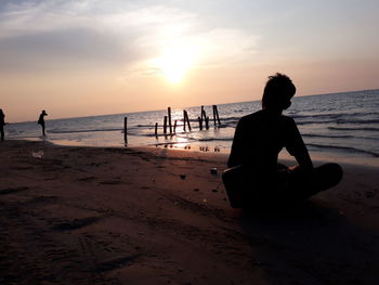 Silhouette people on beach against sky during sunset