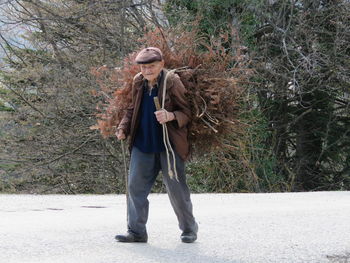 Full length portrait of man carrying dried plants while walking on snow