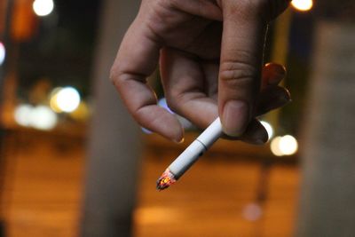 Close-up of hand holding cigarette at night