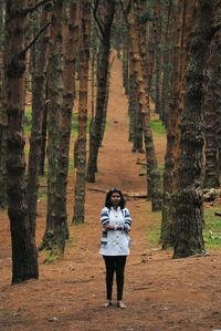 Full length of young woman standing amidst trees at forest